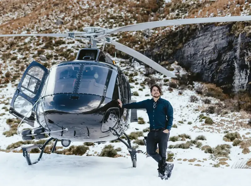 Cristian Batista next to helicopter in snow-covered Queenstown mountains